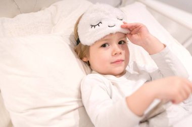 Maske takan yakışıklı bir çocuğun portresi. Cep telefonu kullanarak yatakta uyuyor..