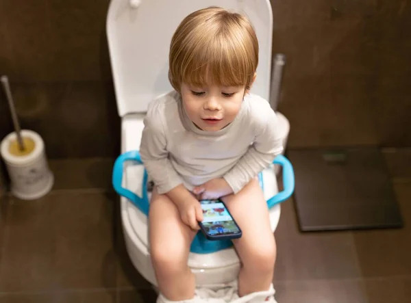 かわいい幼児の男の子 トイレに座って 携帯電話を使って — ストック写真