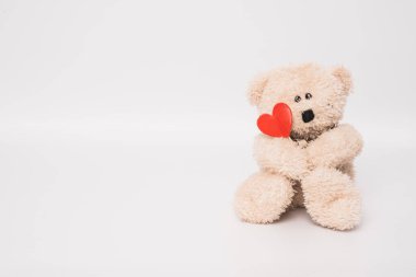 Oyuncak ayının elinde beyaz arka planda izole edilmiş kırmızı bir kalp var. Aşk konsepti.