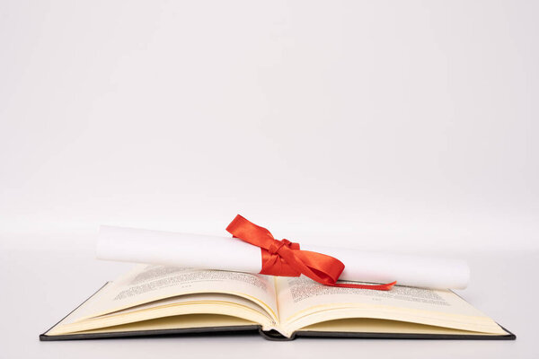 education, school, graduation and knowledge concept - close up of open book and diploma isolated over white background.