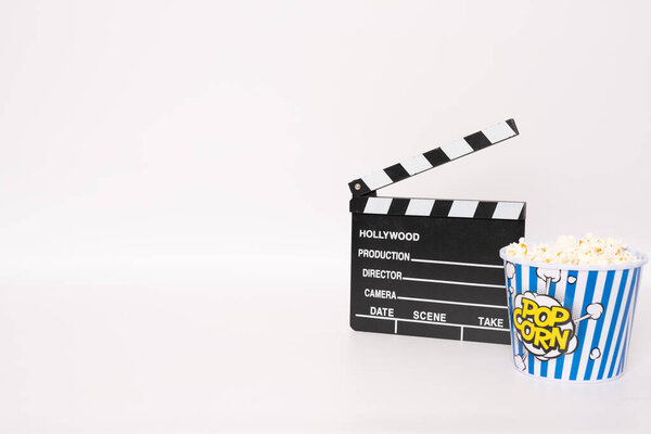 Black Clapper board or movie slate and popcorn over white background.