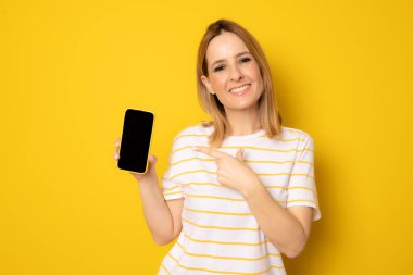 Sarı arka planda izole akıllı telefon gösteren güzel bir genç kadının portresi.