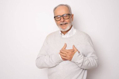 Gri saçlı, gözlüklü, gözlüklü, beyaz, soyutlanmış arka planda duran, elleri göğsünde, gözleri kapalı ve yüzünde minnet dolu bir jest. Sağlık kavramı.