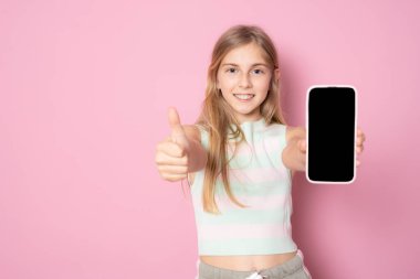 Gülümseyen küçük kız pembe arka planda izole edilmiş boş ekran akıllı telefonu gösteriyor..