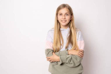 Kollarını kavuşturup beyaz bir arka planda izole edilmiş mutlu küçük bir kızın portresi.