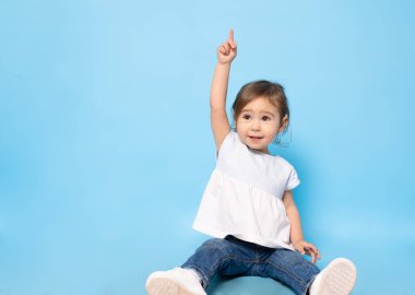 2 yaşında bir çocuk yerde oturuyor ve mavi arka planı işaret ediyor..