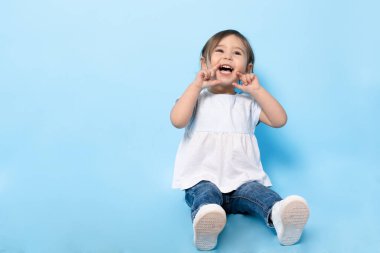 2 yaşında bir çocuk mavi arka planda yerde oturuyor..