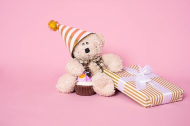 Pembe arka planda hediye kutusu olan sevimli bir oyuncak ayı. Doğum günü kutlaması konsepti.