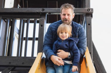 Babasıyla birlikte dışarıda oyun parkında slaytta oynayan sevimli bir çocuk. Babalık kavramı.