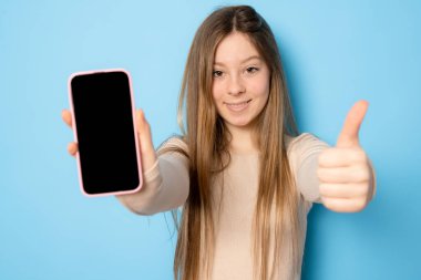 Boş cep telefonu ekranı gösteren ve memnun görünen şık bir kız, akıllı telefon için tavsiye edilen bir uygulama, mavi arkaplan üzerinde alışveriş sitesi gösterimi