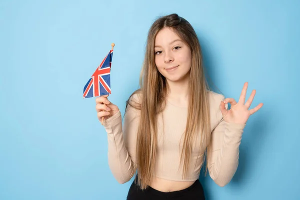 高举英国国旗 欢度节日 看镜头的心满意足的女孩的画像 室内拍摄被蓝色背景隔离 — 图库照片