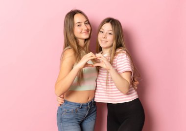 Sonsuza dek arkadaşız. İki sevimli kız arkadaş pembe arka planda kalp figürü oluşturuyorlar.