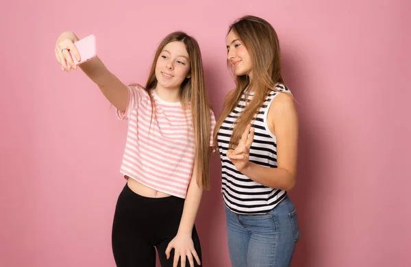 Dvě Veselé Mladé Dívky Mluví Selfie Přes Růžové Pozadí — Stock fotografie
