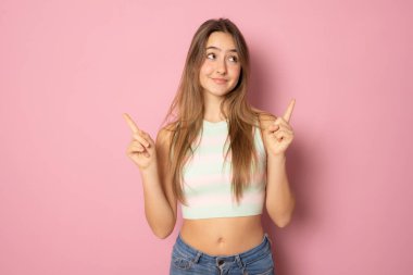 Mutlu genç bir kızın portresi, günlük giysiler giyip pembe arka planda izole edilmiş fotokopi alanını işaret ediyor.