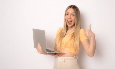 Diz üstü bilgisayar kullanarak beyaz arka planda yalnız duran neşeli, şaşkın genç bir kadın görüntüsü. Kameraya bak.