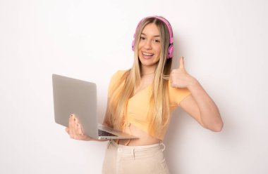 Kulaklık takan, beyaz arka planda dizüstü bilgisayarla izole edilmiş neşeli genç bir kadın görüntüsü. Kameraya bak.