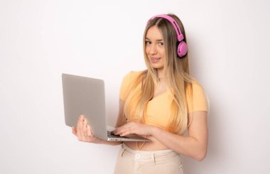 Kulaklık takan neşeli genç bir kadının beyaz arka planda dizüstü bilgisayarla izole edilmiş görüntüsü. Kameraya bak.