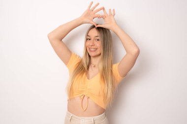 Çekici genç beyaz kız mutlu hissediyor ve romantik şekiller kalp jestleri beyaz arka plana karşı hassas duruşlar sergiliyor. İnsanlar sevgi ve ilgi kavramları.