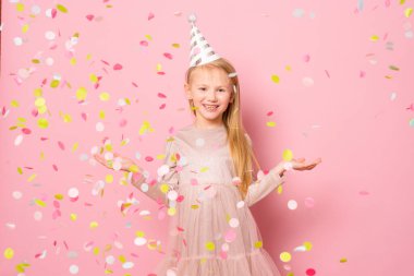 Küçük mutlu genç kız pembe arka planda konfetiyle parti yapıyor..