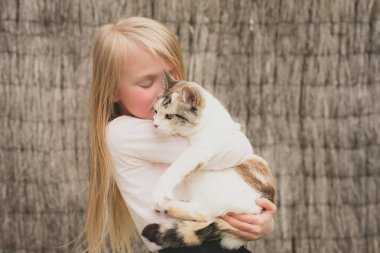 Mutlu küçük güzel kız dışarıda bir kediyi kollarında tutuyor.
