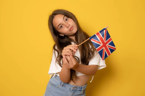 美丽的少女手持英国国旗 庆祝节日 看着相机 穿着白色休闲装T恤的肖像 在黄色背景下隔离的室内拍摄 — 图库照片