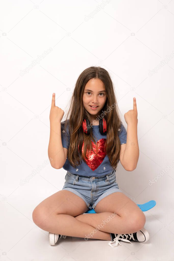 Young brunette girl isolated on white background sitting in a skate and pointing fingers up.