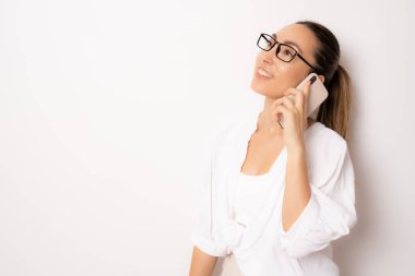 Beyaz arka planda akıllı telefon kullanan gülümseyen bir iş kadını. Beyaz gömlek ve gözlük takıyordu..