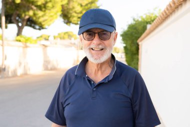 Yaşlı, kır saçlı, gülümseyen adam şehirde mutlu bir şekilde duruyor..