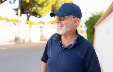 Yaşlı, kır saçlı, gülümseyen adam şehirde mutlu bir şekilde duruyor..