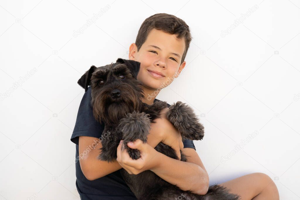 Smiling boy in casual clothing sitting on the grass hugging his dog.