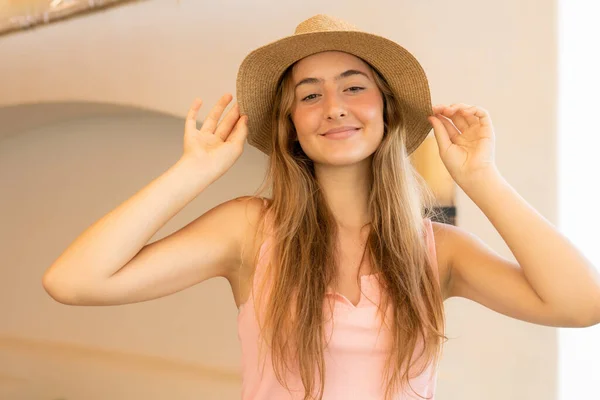 Cute young woman with shining smile, has tanned healthy skin and appealing look, enjoys summer rest in paradise place, wears straw hat, smiles pleasantly. People, beauty and seasonal rest concept