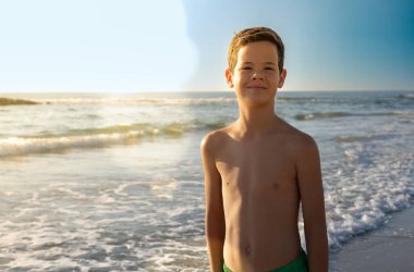 Denize yakın duran mayolu, gülümseyen bir çocuk. Yaz mevsimi kavramı.