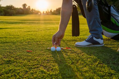 Golfçü golf topunu çimlerin üzerine koy. Güneş ışığı yeşil golf sahası arka planında.,