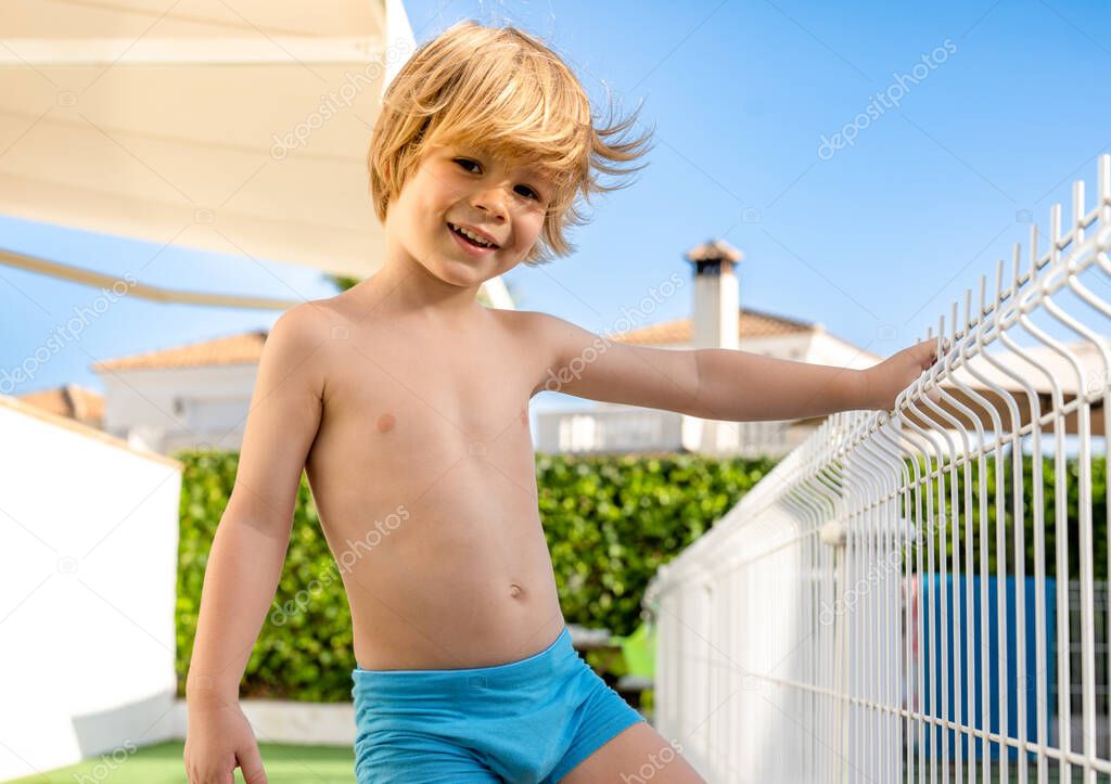 joyful cheerful blond haired little boy stands near the pool on summer vacation.