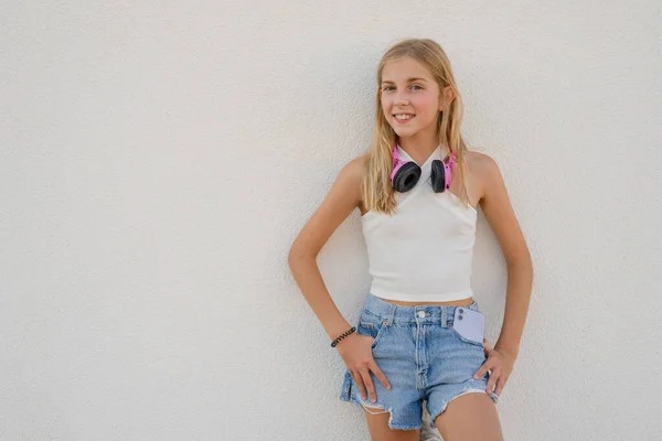 Beautiful little blonde kid girl 12-13 years old in casual clothing posing isolated on white wall children portrait. Childhood lifestyle concept. Mock up copy space. Hold blue skateboard
