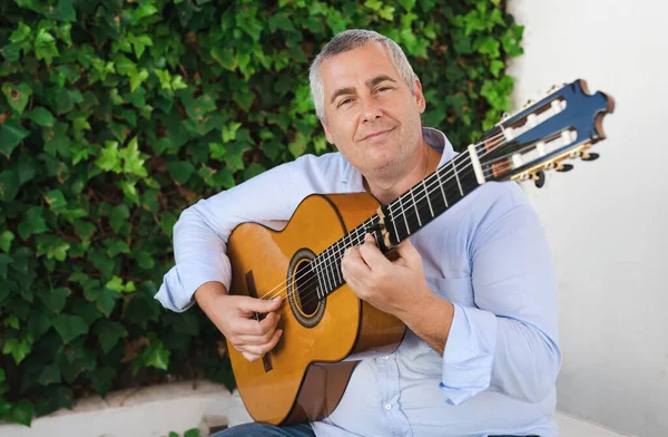 Musician man sitting in a terrace with garden, feels the music while playing