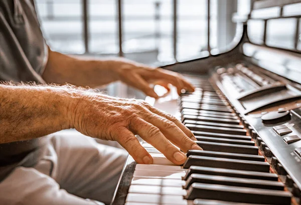 Old person\'s hands playing the piano. Close up view of skin texture and piano keys.