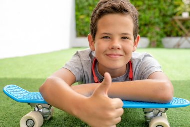 Happy boy lying with his skateboard in the garden of his house