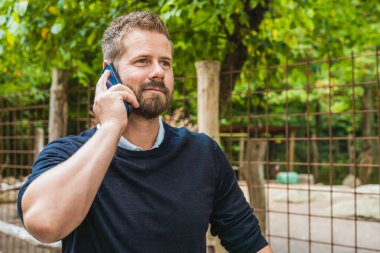 Happy young handsome caucasian hipster man using phone at the park