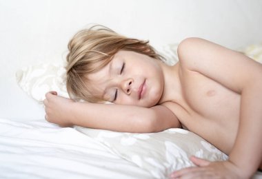 Adorable little blonde boy sleeping in bed