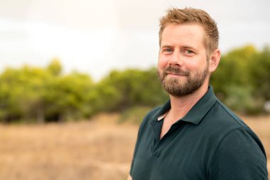 Parkta gülümseyen beyaz bir adamın yakın çekimi.