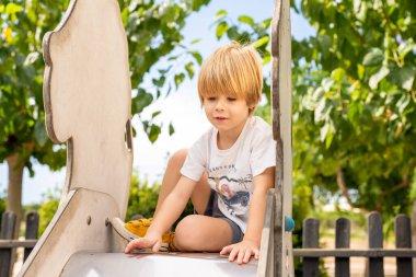 Parktaki salıncakta salıncağa bakan beyaz bir çocuğun portresi.