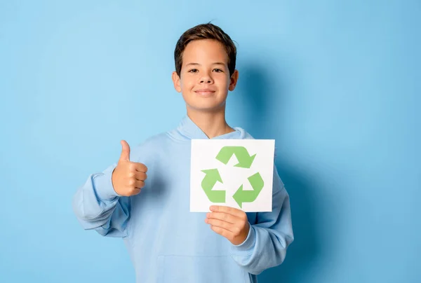 eco living, environment and sustainability concept - smiling boy holding green recycling sign and showing thumb up gesture over blue background