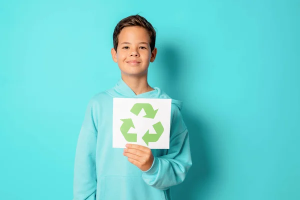 Child boy holding recycling symbol paper standing isolated over green background.. Recycling concept.