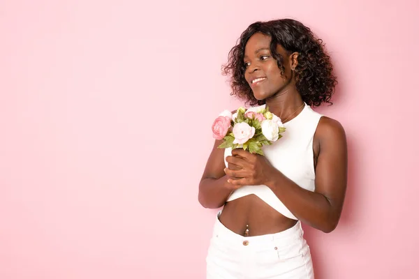 people and international women\'s day concept - happy african american young woman with bunch of peony flowers over pink background