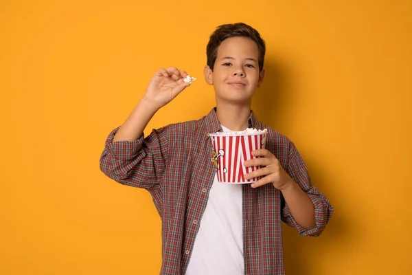 かわいい子供の男の子食べるポップコーン立って隔離されたオレンジの背景 — ストック写真