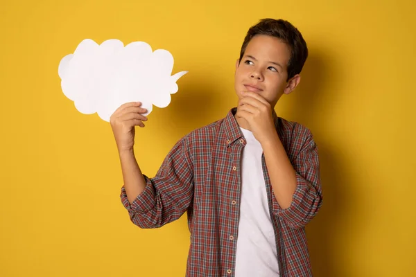 Great Idea. Doubtful boy holding speech bubble with copy space standing isolated over yellow background.