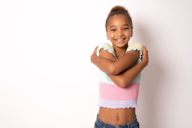 Kendimi seviyorum. Memnun genç Afro-Amerikan kızının portresi. Beyaz arka planda kendini kucaklıyor ve gülümsüyor..