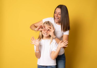 Güzel anne ve kız mutlu bir şekilde gülümsüyor izole edilmiş sarı arka planda birlikte eğleniyorlar..