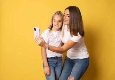 Selfie çeken kadın tatlı bir kızla eğleniyor. Anne, küçük kız sarı arka planda izole edilmiş, stüdyo portresi. Anneler Günü, aile kavramını seviyorum.